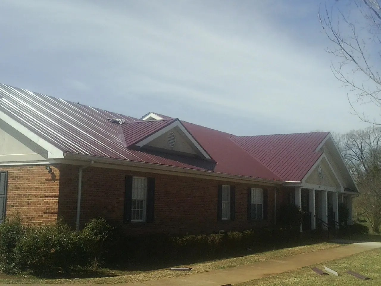 Red metal roof with gabled entries on a long brick building, from a Hail Damage Roof Repair job in Richards