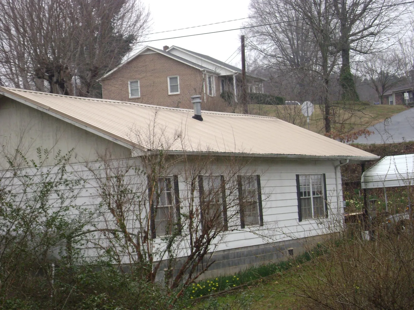 Tan metal roof on a white sided house set into a hillside — Commercial Roofing by Roofing Brothers in Richards